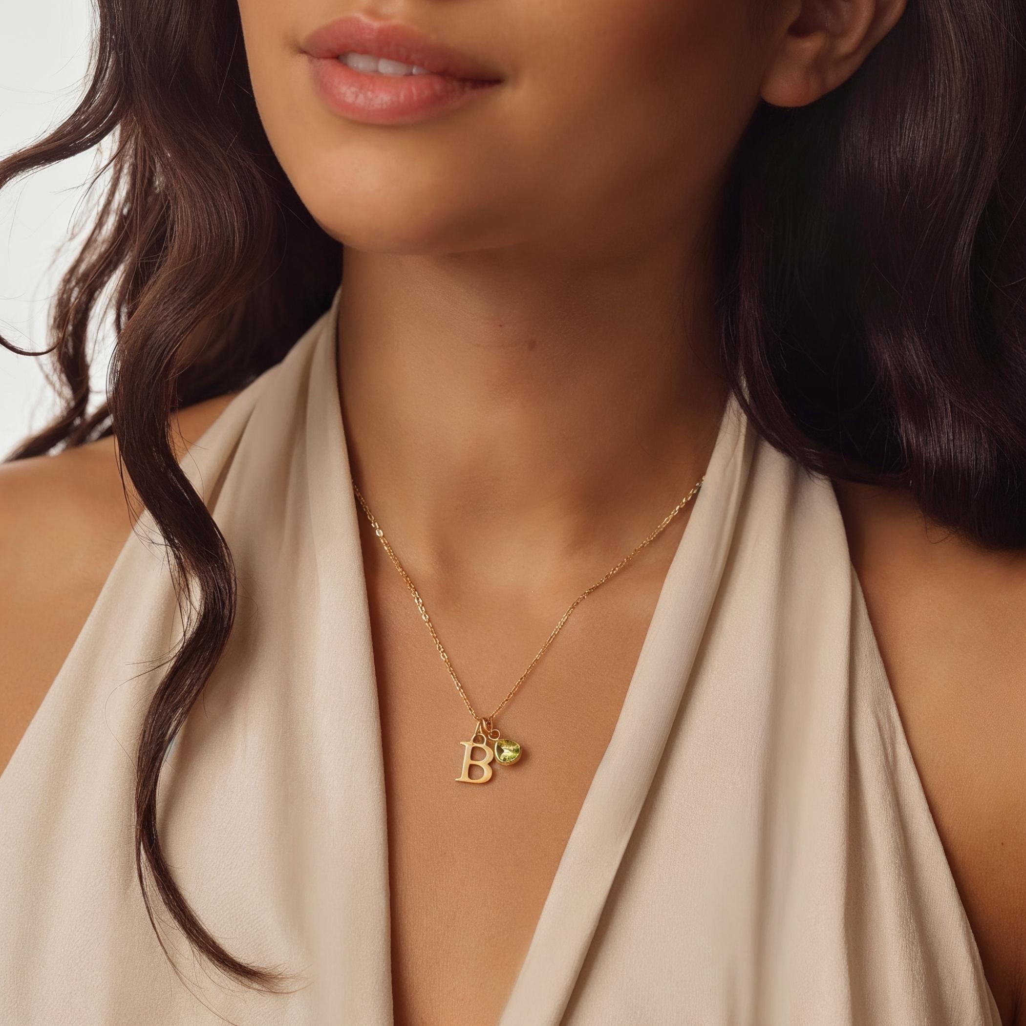 Close-up of a woman wearing a gold birthstone necklace with a 'B' pendant.