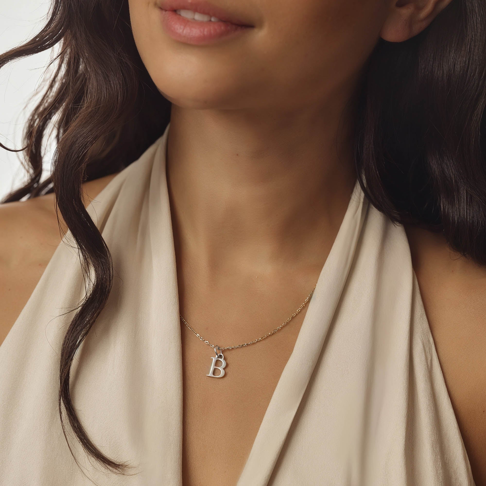 Necklace with a 'B' pendant worn by a person in a beige top.