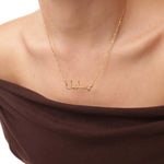 Gold necklace with Arabic script on a person wearing a brown top.