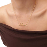 Gold necklace with Arabic script on a person wearing a brown top.