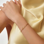 Gold arabic name bracelet on a wrist with a soft yellow fabric background