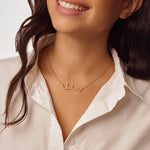 Woman wearing a gold arabic name necklace on a neutral background