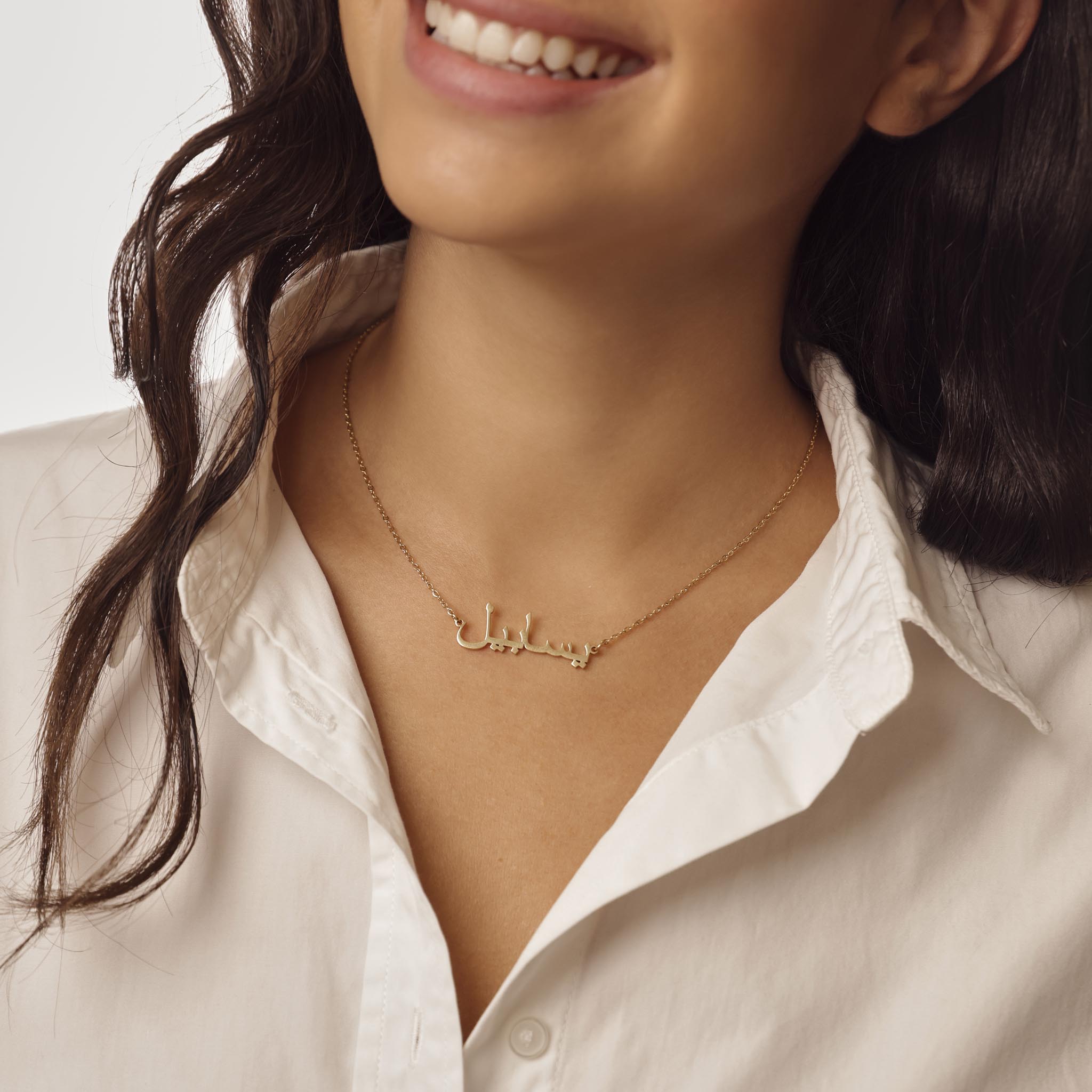 Woman wearing a gold arabic name necklace on a neutral background