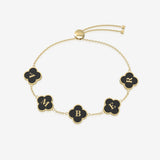 Gold bracelet with black clover-shaped charms displaying letters on a white background