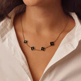 Necklace with black clover pendants worn by a person in a white shirt.