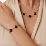 Necklace and bracelet with black clover-shaped charms on a neutral background