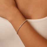 Delicate classic tennis bracelet on a wrist with a neutral background