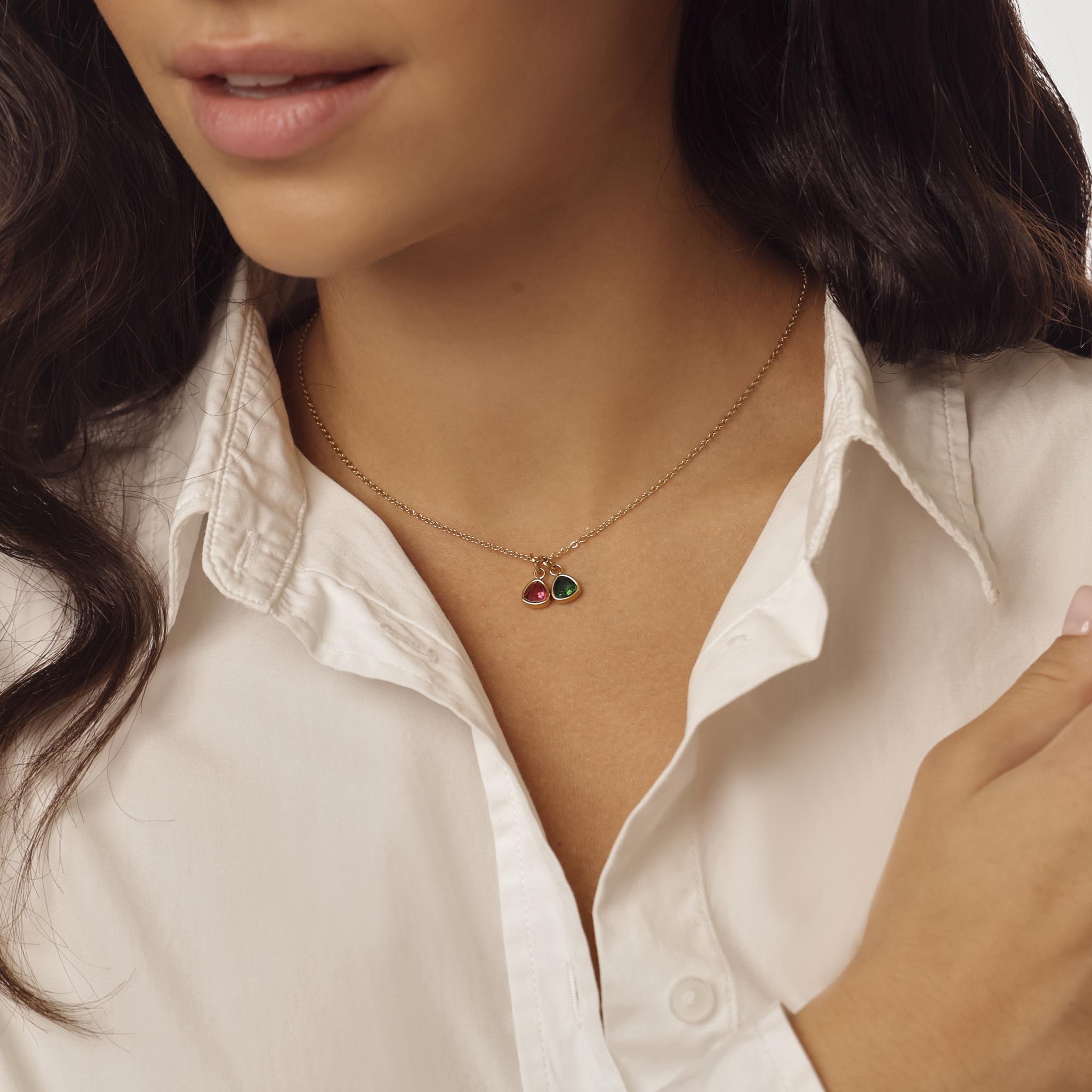 Close-up of a person wearing a delicate necklace with small birthstone pendants against a neutral background
