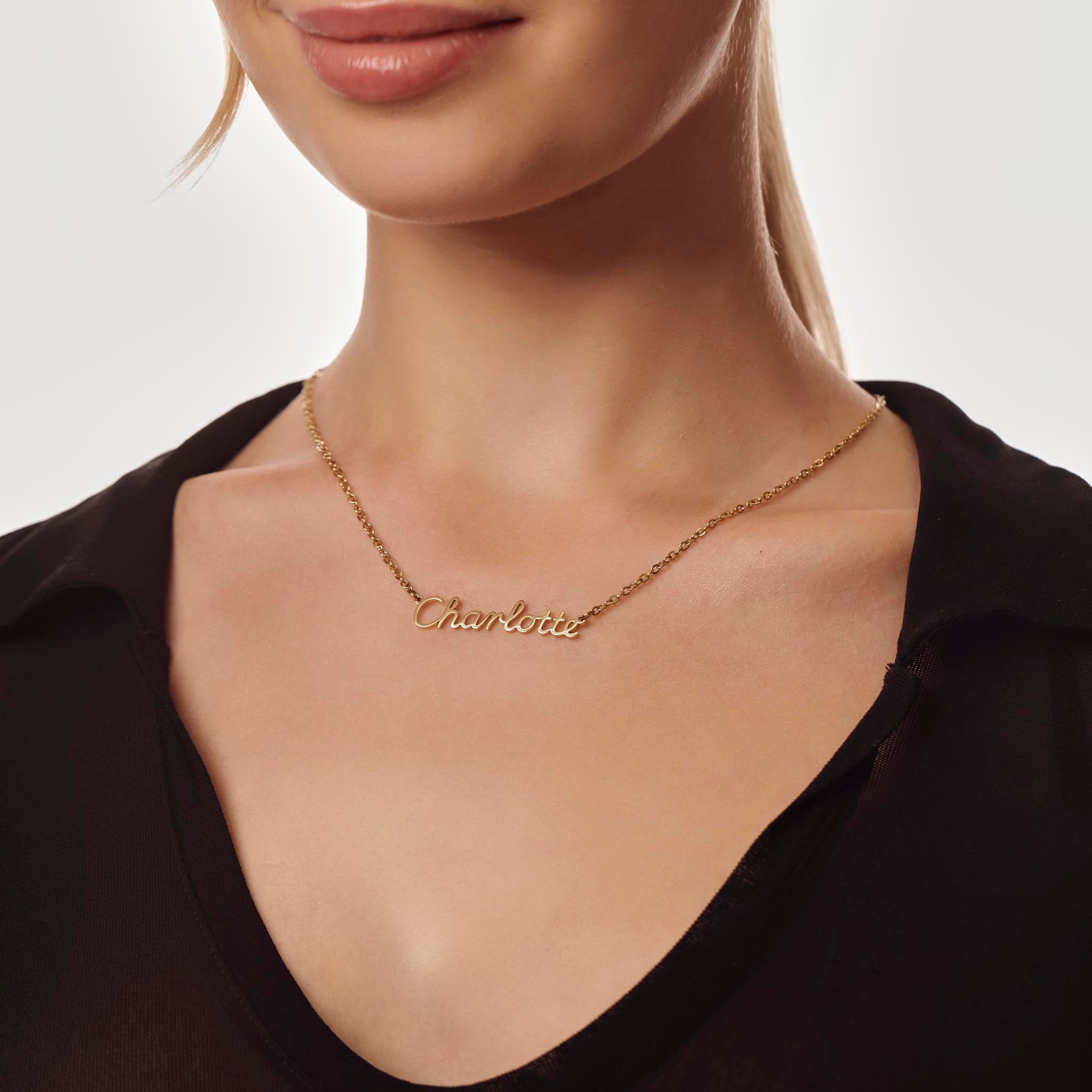 Gold necklace with 'Charlotte' engraving on a person wearing a black top against a neutral background