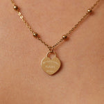 Gold necklace with a heart-shaped pendant on a beige background