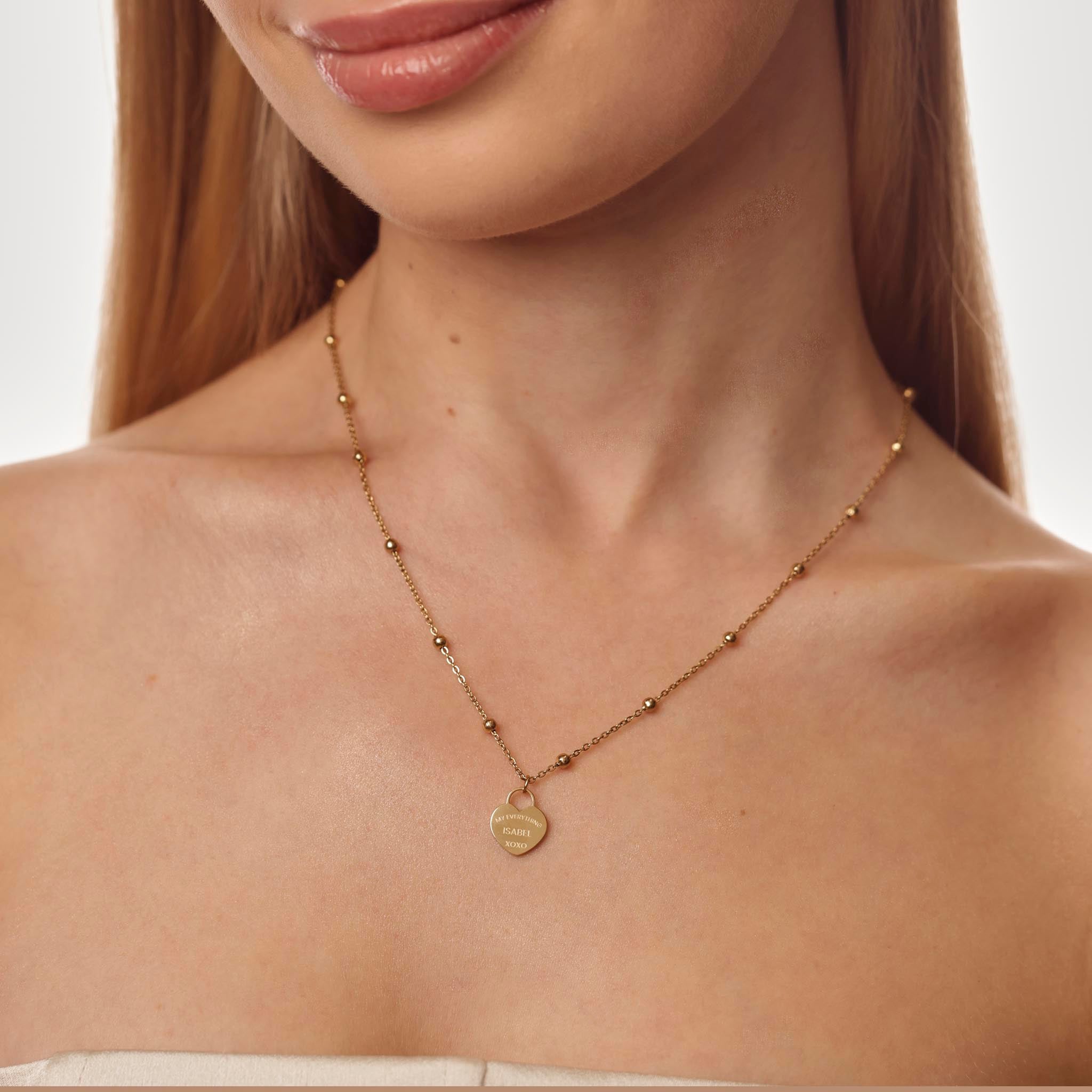 Gold necklace with a heart-shaped pendant on a model against a neutral background