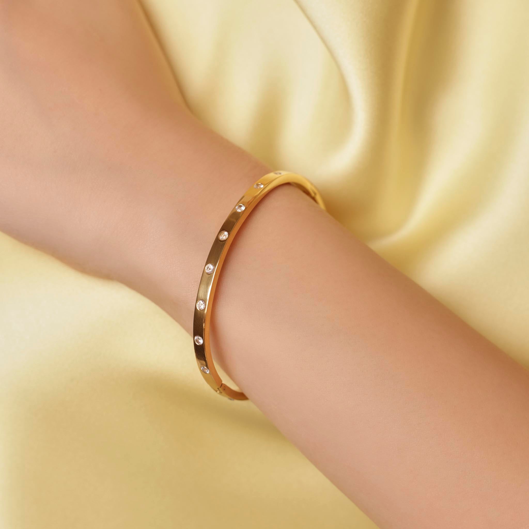 Gold eternity bangle with small diamonds on a wrist against a yellow fabric background