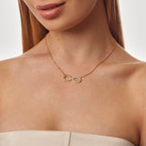 Gold necklace with an infinity symbol worn by a model on a neutral background