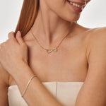 Woman wearing a gold necklace with an infinity symbol on a plain background