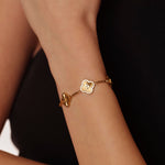 Gold bracelet with a clover design on a wrist against a dark background