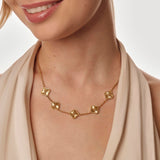 Gold necklace with clover pendants worn by a person against a neutral background