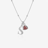 Silver necklace with 'S' pendant and red birthstone charm on a white background