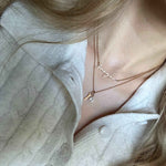 Close-up of a person wearing a delicate necklace with a Isabel Carter necklace stack against a neutral background.