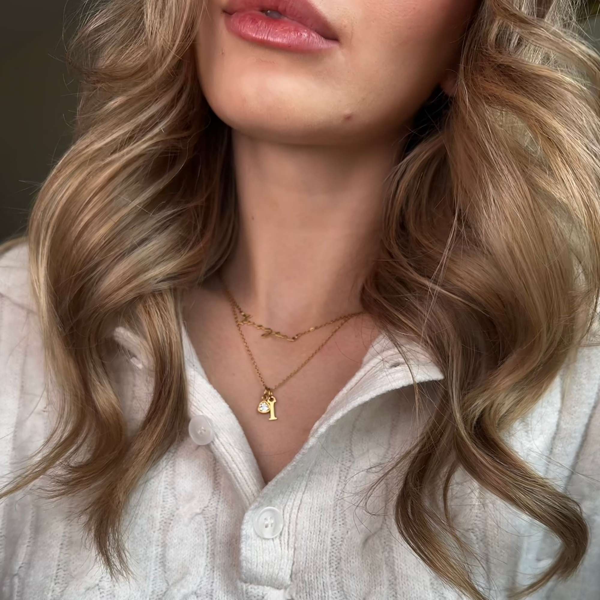 Close-up of a person with wavy blonde hair wearing a white blouse and gold Isabel Carter necklaces.