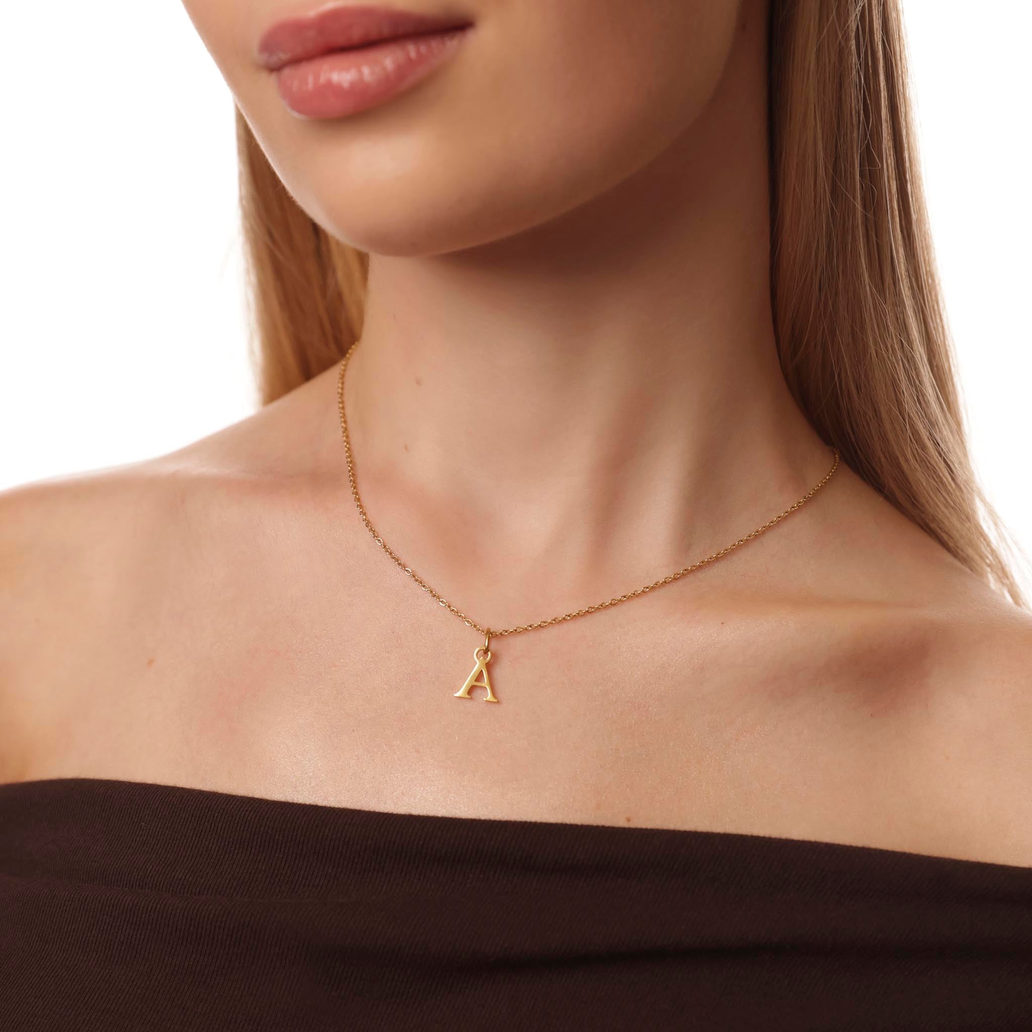 Gold necklace with a letter 'A' pendant on a model against a neutral background