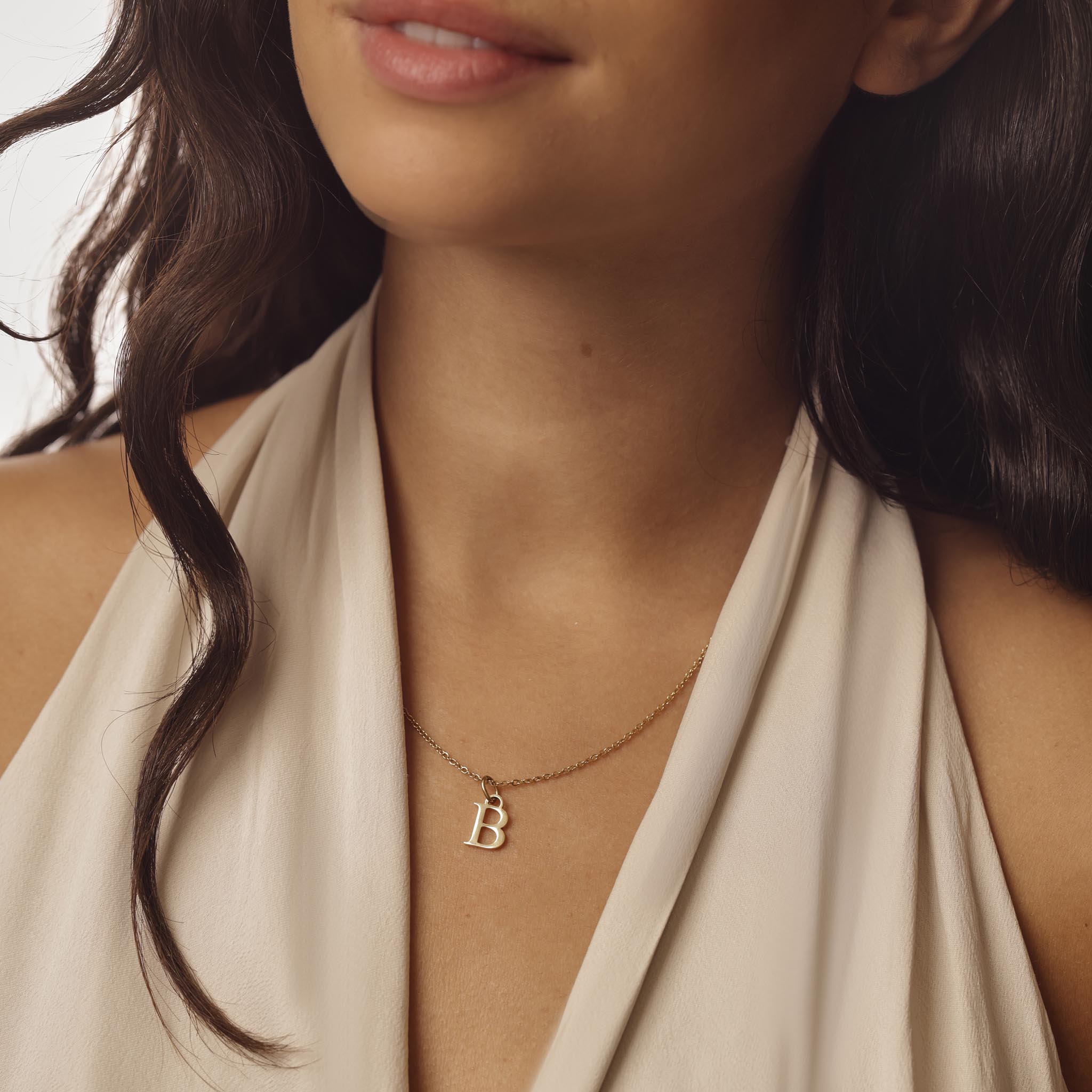 Close-up of a woman wearing a gold necklace with a 'B' pendant.