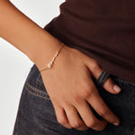 Hand wearing a gold bracelet with a Mama design on a plain background