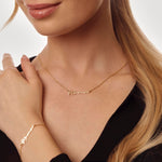 Close-up of a person wearing a gold mama necklace and bracelet on a neutral background