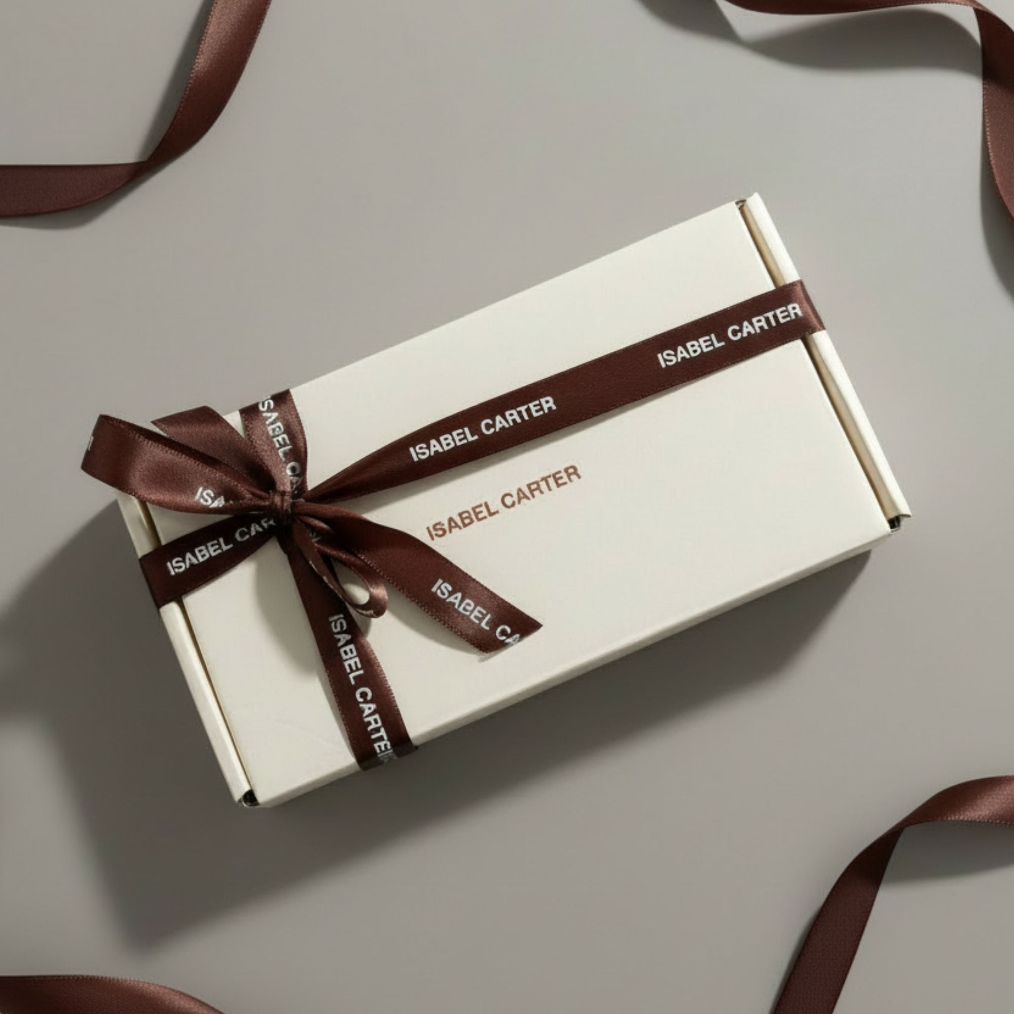White gift box with brown ribbon and 'Isabel Carter' branding on a light gray background
