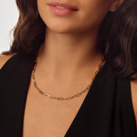 Close-up of a person wearing a gold paperclip chain necklace against a neutral background