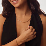 Woman wearing a gold paperclip necklace and paperclip bracelet against a neutral background