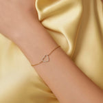 Gold bracelet with a heart design on a wrist against a yellow satin background