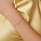 Gold bracelet with a heart design on a wrist against a yellow satin background