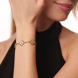 Gold bracelet with clover designs on a person's wrist against a neutral background