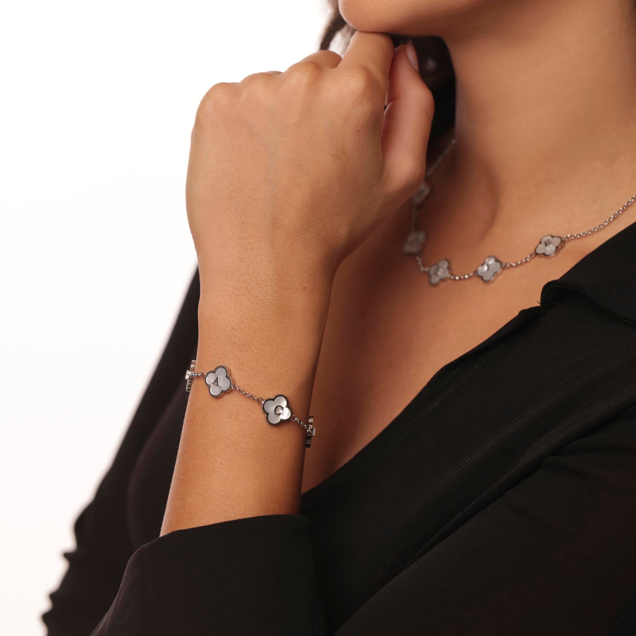 Person wearing a silver clover bracelet with name designs on a plain background
