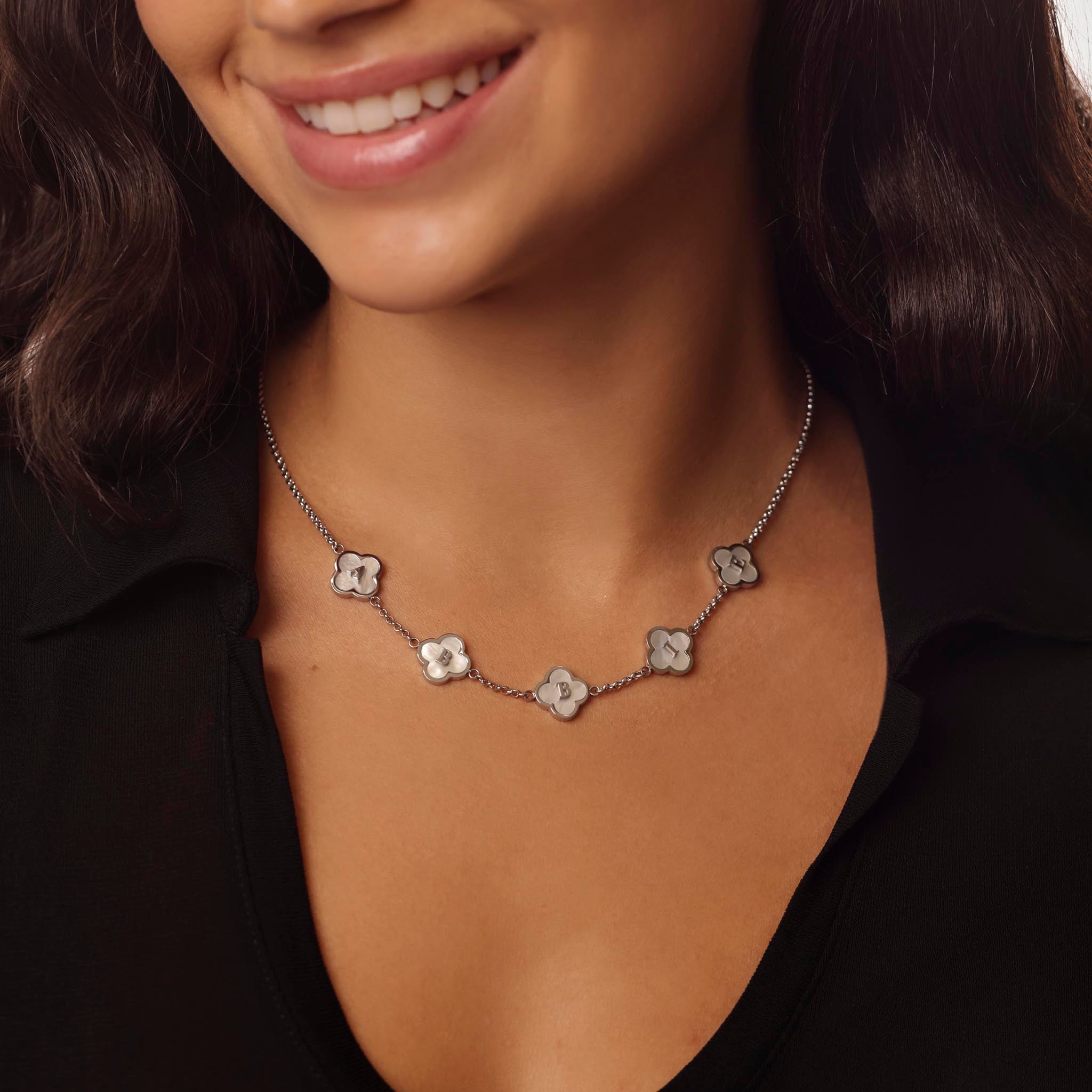 Close-up of a woman wearing a silver clover necklace against a neutral background