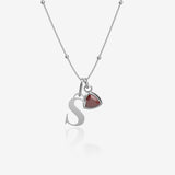 Silver necklace with 'S' pendant and red birthstone charm on a white background