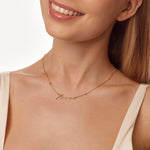 Close-up of a woman wearing a gold name necklace with a neutral background