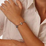 Close-up of a person wearing a silver clover bracelet on a white shirt background