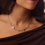 Silver clover necklace worn by a person with a dark background