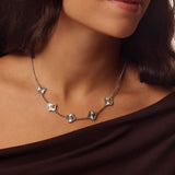 Silver clover necklace worn by a person with a dark background