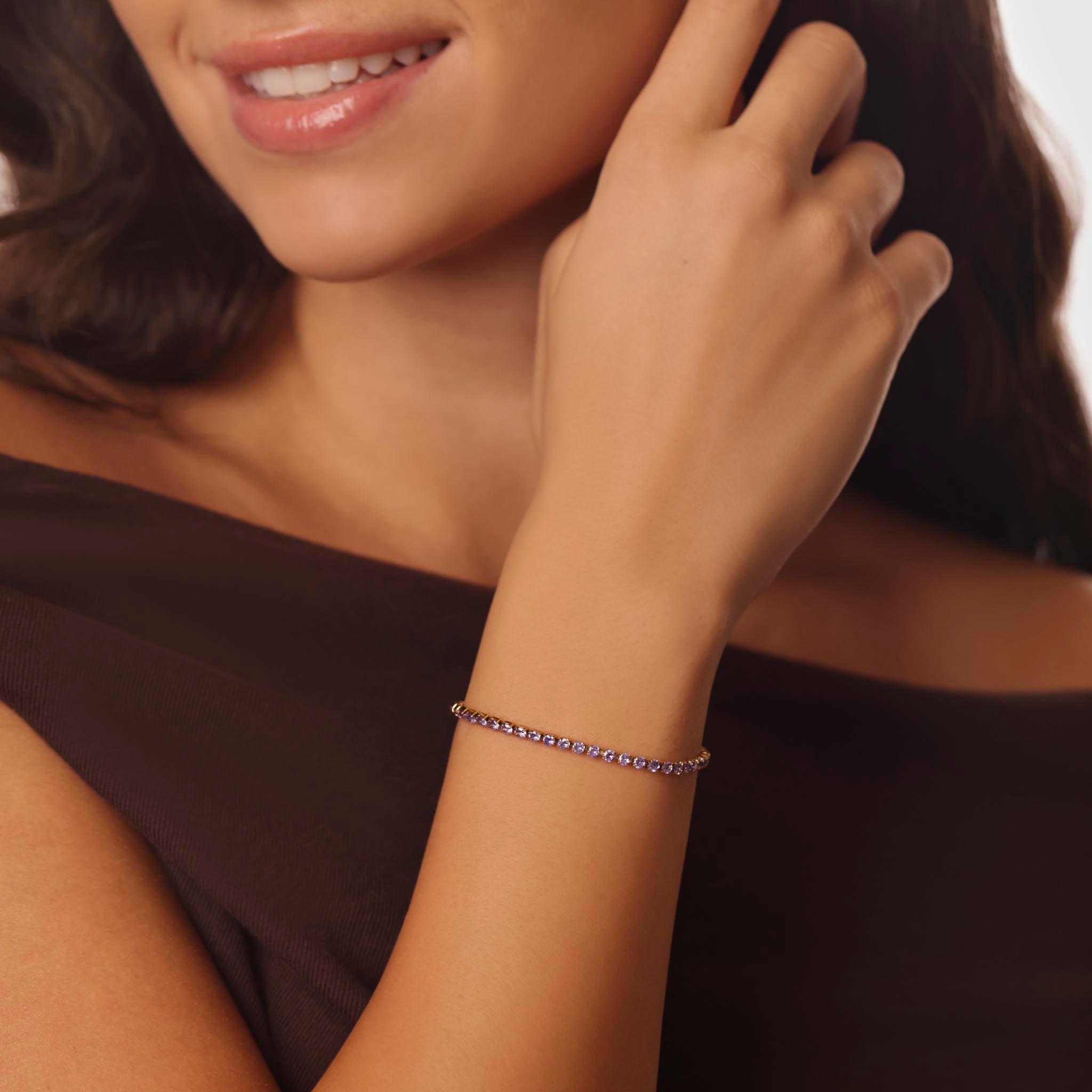 Close-up of a woman wearing a amethyst birthstone tennis bracelet on a neutral background
