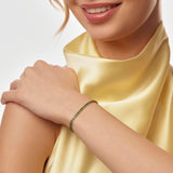 Woman wearing a yellow top and a emerald birthstone tennis bracelet on a plain background