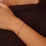 gold ruby birthstone tennis bracelet on a wrist against a dark background