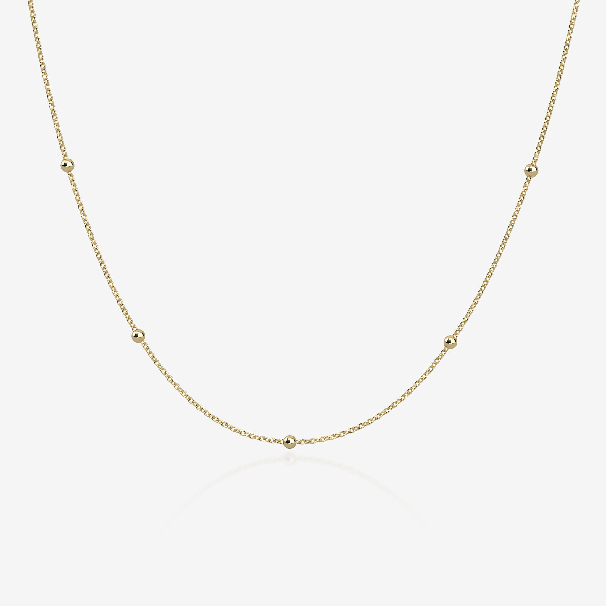Gold ball chain necklace on a light beige background